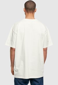 Balta, per didelė T-shirt marškinėliai trumpomis rankovėmis, pagaminti iš minkštos medvilnės. Turi laisvą siluetą ir paprastą, vientisą dizainą be dekoracijų.