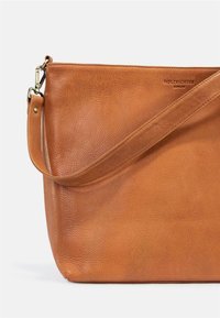 Tan leather shoulder bag with a textured finish, featuring a long strap and embossed logo detail on the side. Smooth interior surface.