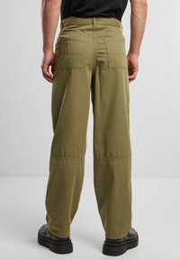 Pantalones cargo de algodón verde oliva con un corte relajado, que cuentan con dos bolsillos traseros, costuras indistintas y un diseño de pierna recta. Calzado negro visible.