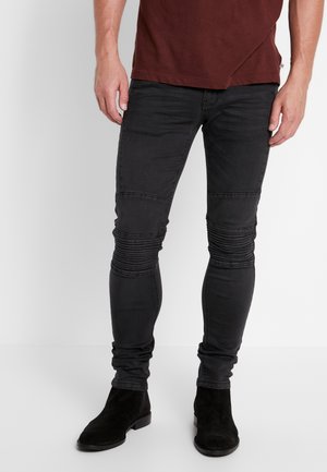 Jeans skinny neri con dettagli a coste sulle ginocchia e una texture liscia, abbinati a stivaletti neri in suede.