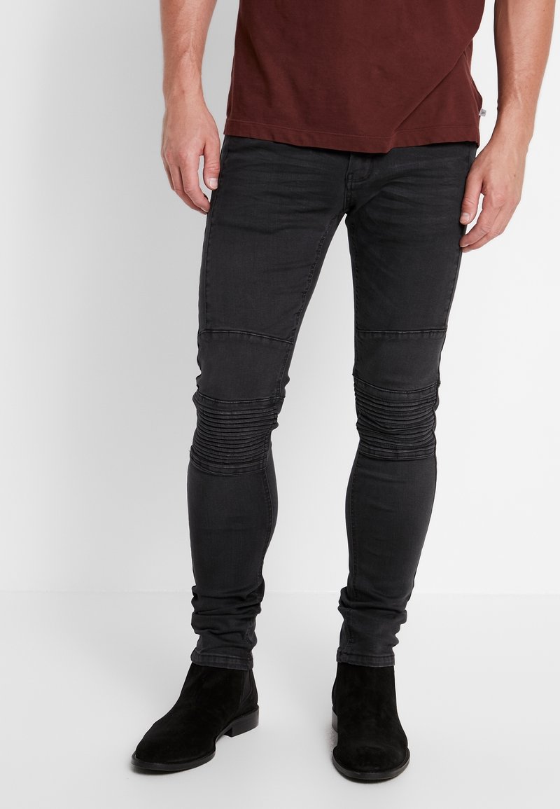 Černé skinny džíny s vroubkovanými detaily na kolenou a hladkým povrchem, doplněné černými semišovými kotníkovými botami.