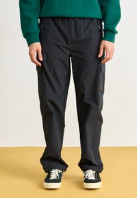 Zwarte cargobroek met een relaxed fit, gemaakt van lichtgewicht materiaal, met zijzakken en een trekkoord in de taille, gecombineerd met donkere schoenen.