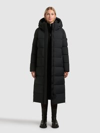 Črna dolga puffer jakna s kapuco, kvadratna zasnova, prešita tekstura, sprednji zadrga in gumbki na ježka, v kombinaciji s črnimi gležnjarji.