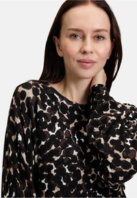 Czarny sweter o luźnym kroju z motywem panterki w odcieniach brązu i kremu. Widoczne są prążkowane wykończenia kołnierza i mankietów.