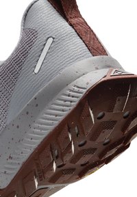 Close-up of gray and brown trail running shoe sole with textured tread and speckled midsole design.