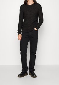 Camicia nera a maniche lunghe con texture, abbinata a pantaloni neri e scarpe stringate nere, caratterizzata da una vestibilità rilassata e scollo a girocollo.