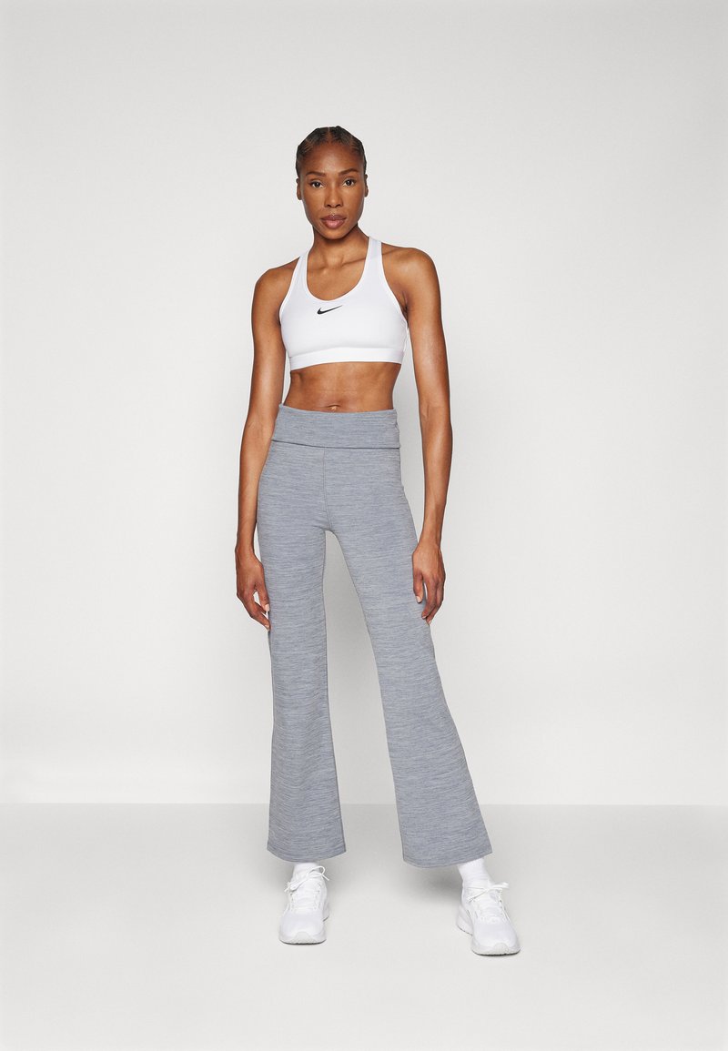 Sport-BH in Weiß mit einem schwarzen Logo, kombiniert mit grauen, ausgestellten Trainingshosen. Beide Stoffe haben eine glatte Textur, die für Komfort und Bewegung ausgelegt ist.