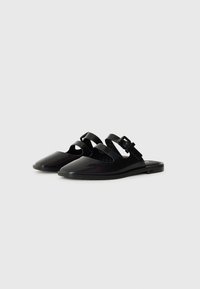 Black slide sandals featuring a glossy finish, open toe design, and two adjustable straps with a buckle for fit. Flat soles, minimalist shape.