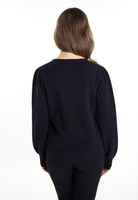 Maglione blu navy con scollo a barchetta, maniche a sbuffo e polsini a coste. Texture morbida, vestibilità comoda, indossato sopra pantaloni neri.