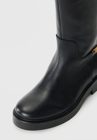 Black leather knee-high boot with a rounded toe and flat sole. Features a side zipper and subtle stitching for added detail.