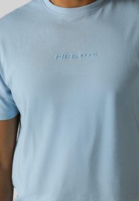 Svijetloplava majica s okruglim izrezom napravljena od glatkog pamuka. Sadrži reljefni logo "BEEPOLICE" u odgovarajućoj boji na prsima.