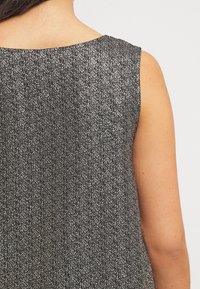 Černý top bez rukávů se stříbrným tečkovaným vzorem, s kulatým výstřihem a volným střihem, který zdůrazňuje jemné vzorové detaily látky.