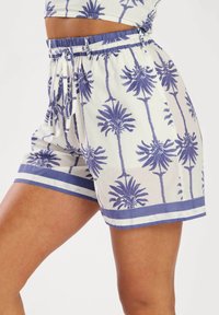 Pantalones cortos de algodón con un fondo blanco y un audaz estampado de palmeras azules. Cintura elástica con cordón, realzada con rayas azules.