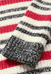 Stickad tyg med horisontella ränder i röd, svart och vit. Tjock textur med ett ribbat mönster och kontrasterande färgkompositioner.