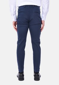 Pantaloni di cotone blu navy con un design affusolato, dotati di due tasche posteriori e una texture liscia, abbinati a scarpe eleganti nere.