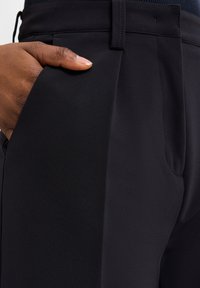 Donkerblauwe broek van gladde stof, met een zijzak en een gestructureerde tailleband met zichtbare stiksels.