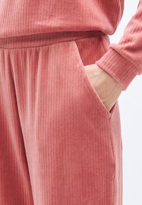 Vêtements d'intérieur côtelés roses avec une coupe décontractée, des poches latérales et un tissu texturé. Les poignets et la taille sont finement finis.