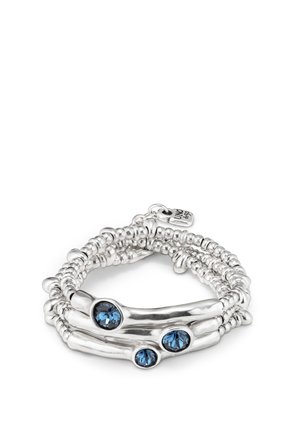 Bracelet multi-brins en argent avec trois pierres précieuses bleues. Sections lisses et texturées se combinent pour un design ondulé aux détails complexes.