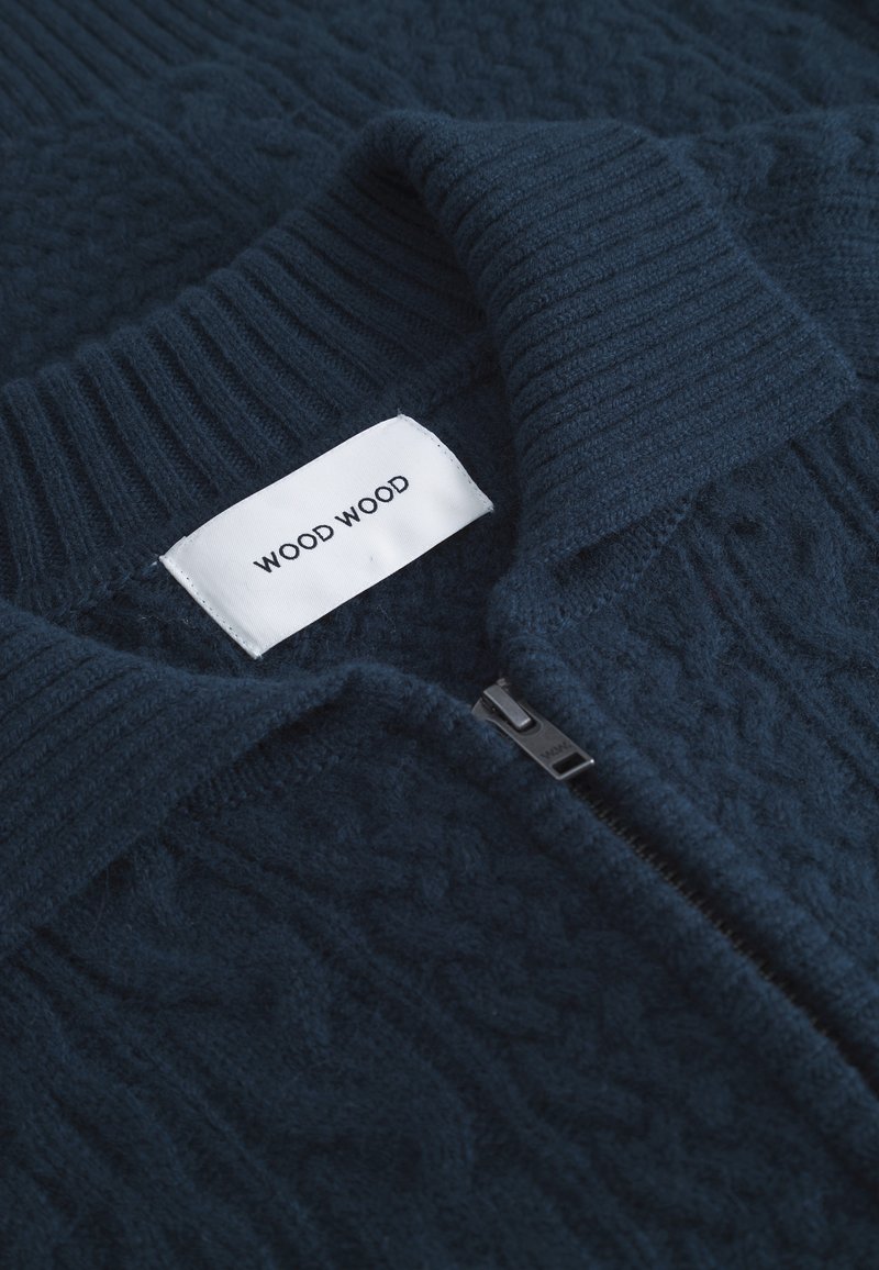 Navyblauer Reißverschluss-Pullover mit geripptem Kragen und strukturiertem Kabelstrickmuster. Das Etikett trägt die Aufschrift "WOOD WOOD." Verfügt über einen schwarzen Reißverschluss.