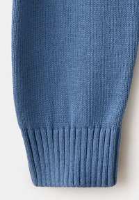 Manche en tissu tricoté bleu avec détail de poignet côtelé, montrant la texture et le motif de points sur un fond clair.