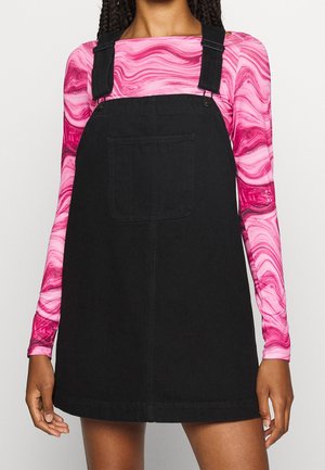 Czarna dżinsowa sukienka ogrodniczka z ramiączkami, z przednią kieszenią, noszona na różowej bluzce z długim rękawem w wirujące wzory.