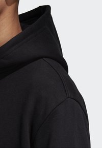 Sudadera negra con capucha, hecha de una tela suave. El detalle en primer plano muestra un diseño de hombro sin costuras y un material texturizado.