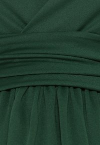 Grön tyg med plisserad textur och horisontella draperingsdetaljer. Materialet verkar mjukt och något strukturerat.