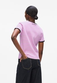 Rosa und weiße gestreifte Kurzarm-T-Shirt mit schwarzem Abschluss und "KARL LAGERFELD"-Branding auf der Rückseite, getragen mit dunklen Denim-Hosen.