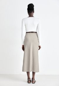 White ribbed long-sleeve top and beige midi skirt. Skirt features a flowing silhouette. Model wears silver sandals. Back view.