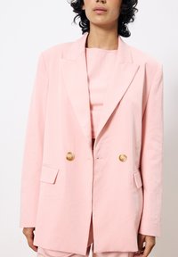 Doppelt knöpfbarer Blazer aus leichtem pinken Baumwollstoff mit goldenen Knöpfen, großen Revers und vorderen Taschen, in entspannter Passform und glatter Textur.
