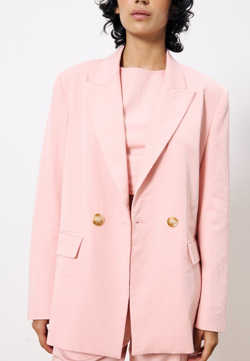 Doppelt knöpfbarer Blazer aus leichtem pinken Baumwollstoff mit goldenen Knöpfen, großen Revers und vorderen Taschen, in entspannter Passform und glatter Textur.