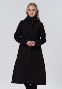 Cappotto da pioggia nero, di lunghezza fino al ginocchio, realizzato in un materiale liscio e impermeabile. Presenta una chiusura frontale con zip, cappuccio regolabile e tasche laterali.