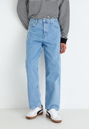 Jean en denim bleu clair avec une coupe droite, style cinq poches et une fermeture à bouton. Porté avec un haut à manches longues rayé noir et blanc.