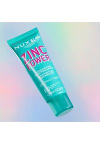 Turkosfärgad presskammare med en teal kork, som har fet rosa text som säger "ZINC POWER." Produktbeskrivning och volyminformation på etiketten.