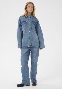 Veste en denim avec une fermeture à boutons sur le devant, deux poches poitrine et une coupe décontractée, associée à un jean assorti avec des accents de boutons sur les côtés.