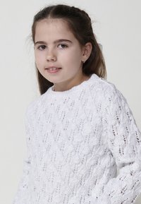 Pull en tricot blanc avec un motif texturé en mailles ajourées et un col rond. Un petit détail de bouton se trouve à l'épaule.