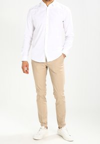 Vit skjorta med knappar som är ihopparad med beige slim-fit byxor och vita sneakers. Slät väv, skräddarsydd design och minimalistisk estetik.