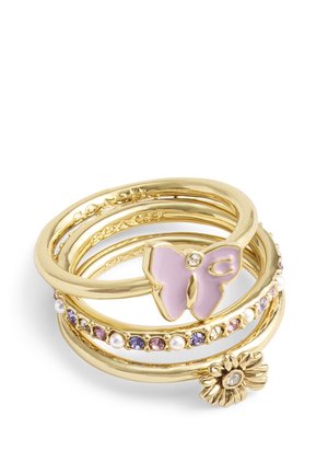 Anillos de oro apilados con una mariposa morada, un charm de flor y pequeñas piedras preciosas moradas y blancas.