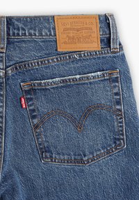 Jeans de denim con una etiqueta de cuero que dice "Levi Strauss & Co." y un característico bolsillo trasero con un diseño arcuado bordado.