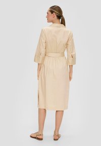 Beiges Baumwollkleid mit Gürtel, 3/4-langen Ärmeln, seitlichen Schlitzen und Kragen. Glatte Textur, taillierte Passform, knielange Schnitt.