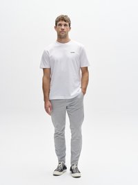 White cotton t-shirt with a black logo, paired with light gray trousers and black sneakers. Simple design, relaxed fit, smooth texture.