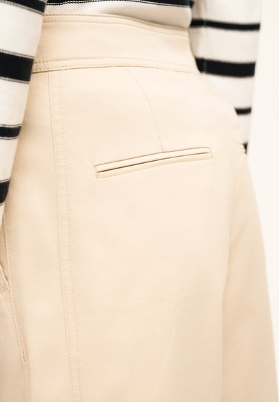 Μπεζ παντελόνι ψηλόμεσο με στενή πίσω τσέπη, φορεμένο με μακρυμάνικη μπλούζα σε ασπρόμαυρες ρίγες.