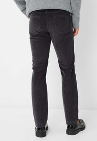 Mørkegrå fløjl-bukser med slim fit, der har synlige teksturerede riller, to baglommer og sorte sko med grov sål.