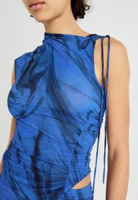 Niebieska marmurkowa sukienka bez rękawów z marszczeniami i wiązaniem na ramieniu. Przezroczysta, lekka tkanina z bocznym wycięciem.