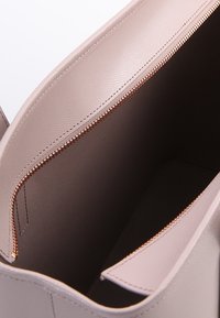 Jasnoróżowa torba na ramię o teksturowanym wykończeniu, złotym suwak i przestronnym wnętrzu wykończonym beżową podszewką.