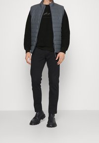 Gilet piumino grigio, maglione in pile nero, pantaloni slim-fit neri e stivali chunky neri. Design semplice; senza fantasie o accenti notevoli.