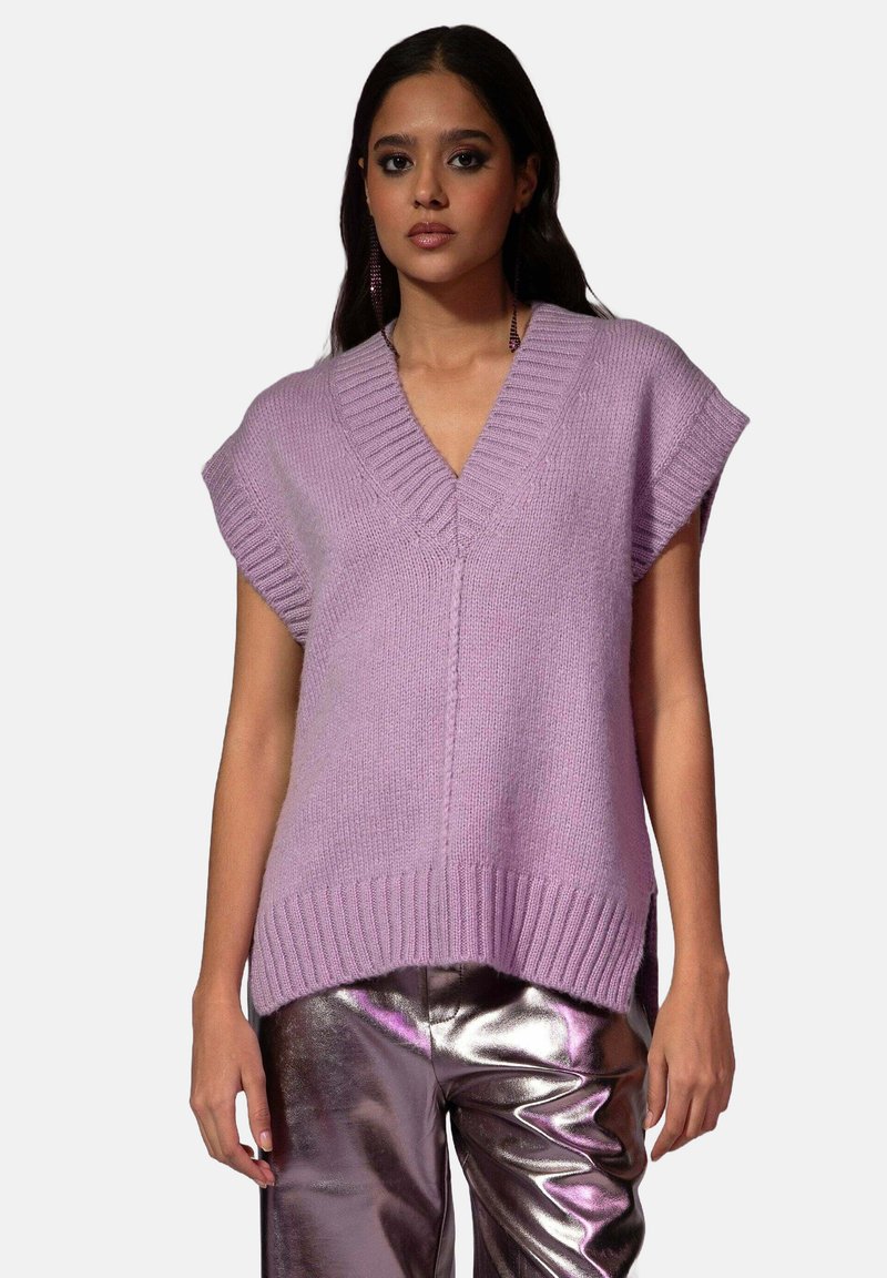 Pull en maille lavande avec un col en V, des manches courtes et un ourlet côtelé. Porté par-dessus un pantalon argenté métallique brillant.