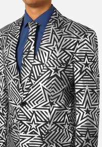 Chaqueta de traje a rayas plateadas y negras con un patrón de estrellas audaz, combinada con una camisa azul real y una corbata a juego. Material texturizado y diseño elegante.