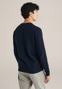 Tengerészkék kötött pulóver, mintás textúrával, környakkal, bordázott mandzsettával és szegéllyel. Világosszürke nadrággal párosítva.