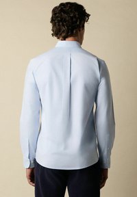Lichtblauw langarmshirt met een gestructureerde kraag, rugplooi en knoopmanchetten. Glad textuur, aansluitend ontwerp, minimale details.